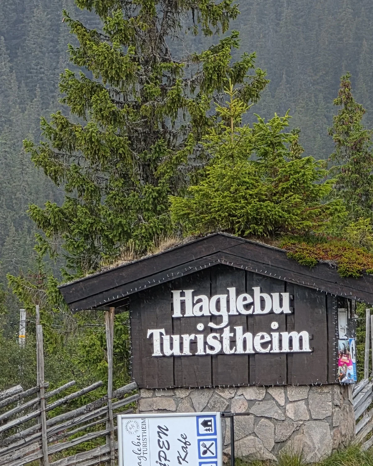 Fasadeskilt med teksten Haglebu Turistheim i skog- og fjellandskapet på Haglebu