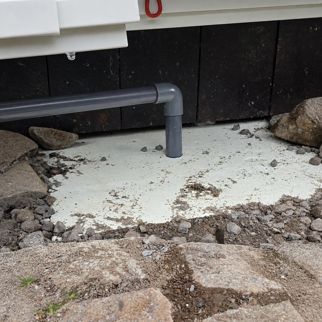 PVC-avløp ført gjennom isolasjon og ned i grunnen under varmepumpens utedel i Kongsberg